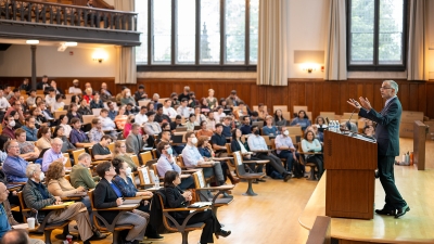 Sanjeev Arora at a podium in front of an audience in a large lecture hall.