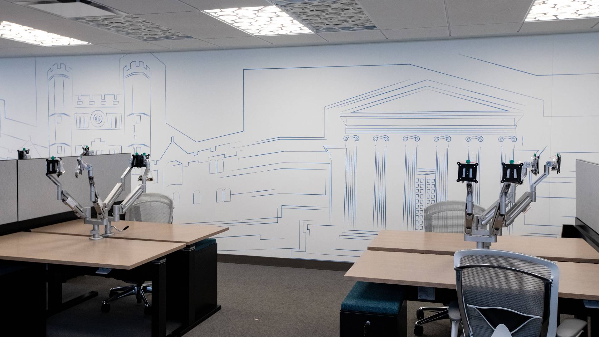 Office interior showing a wall behind desks. The wall has a blue outlined drawing of University buildings.