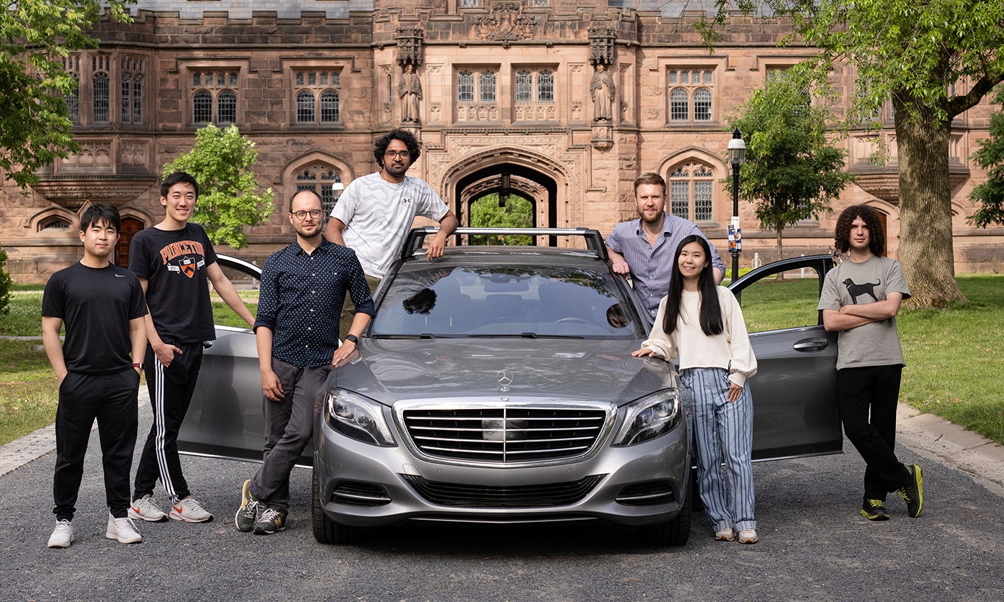 Heide's lab group standing outside on Princeton's campus posing with a test vehicle. The car's doors are open and it's parked on a gravel road.