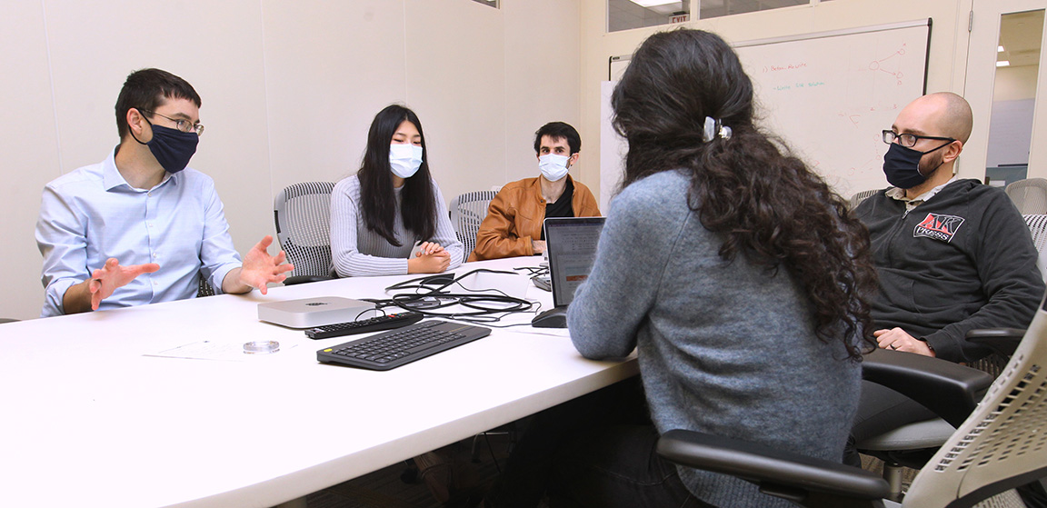 Yuri Pritykin and his lab group sitting around table in a conference room.